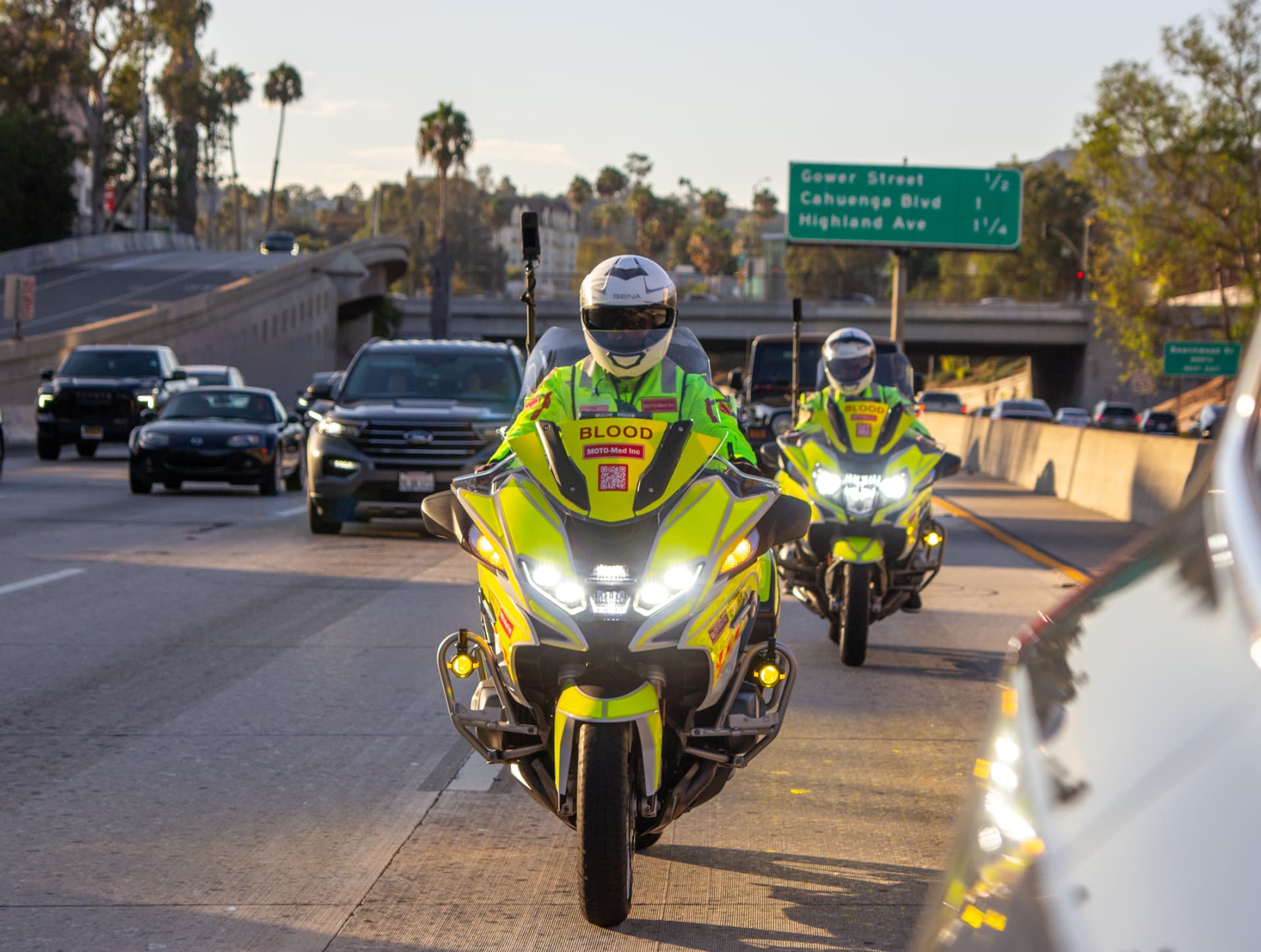 Two Moto-Med riders in hi-vis blood transport gear navigating Los Angeles freeway traffic