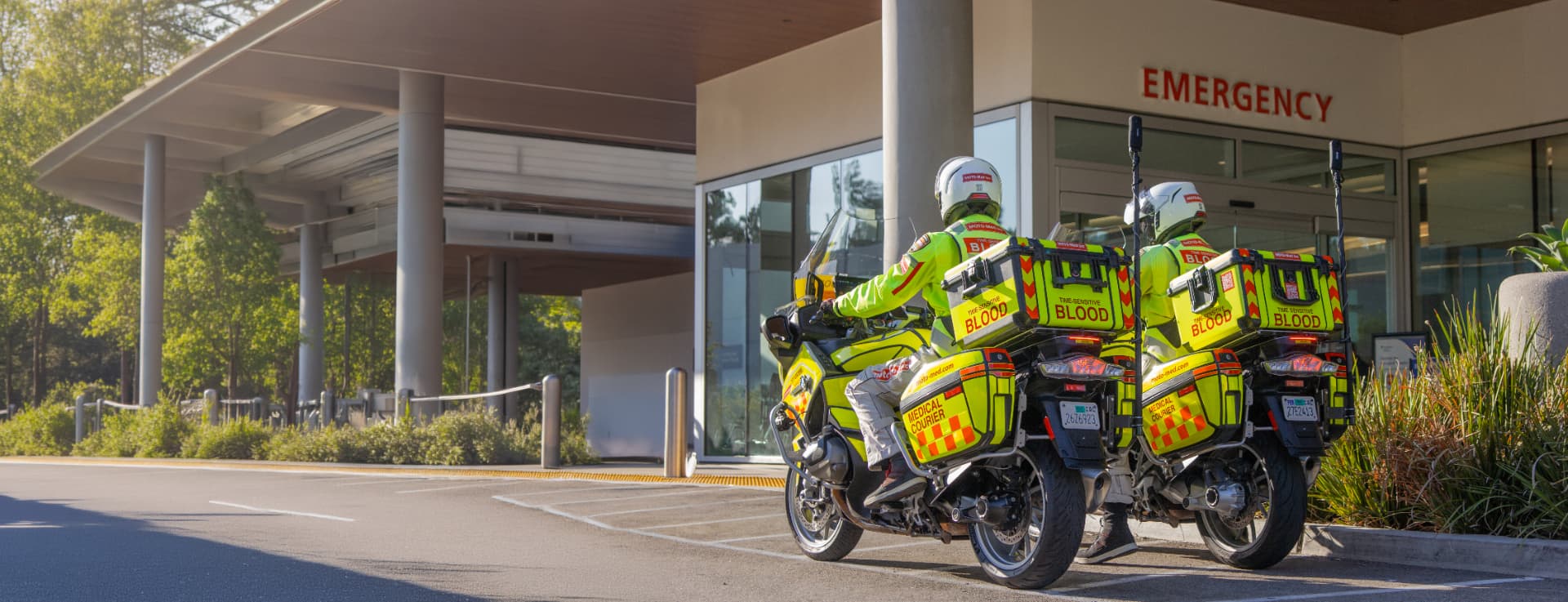 Two Moto-Med riders on hi-vis blood transport motorcycles outside a hospital emergency entrance